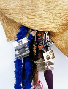 The artist combines a camera, straw, rope, an image of a native woman, and a photo of a white woman, possibly a model or an actress.