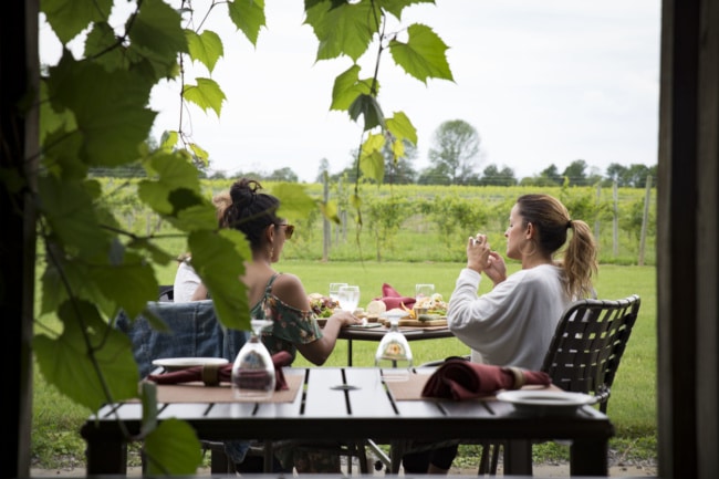 A group enjoys a lunch at a small picnic table while visiting a winery along the Cayuga Wine Trail.