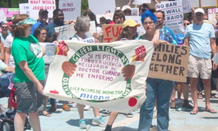 A banner at the Families Belong Together rally from Green Light NY reads, "si mi papa tubiera licencia me llevaria al doctor cuando me enfermo. Licencias de manejar "ahora" Meaning: If my father had a license, he would take me to the doctor when I get sick. Driver's licenses "now"